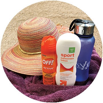 Hat, sunscreen, bug spray, and towel on a sandy beach